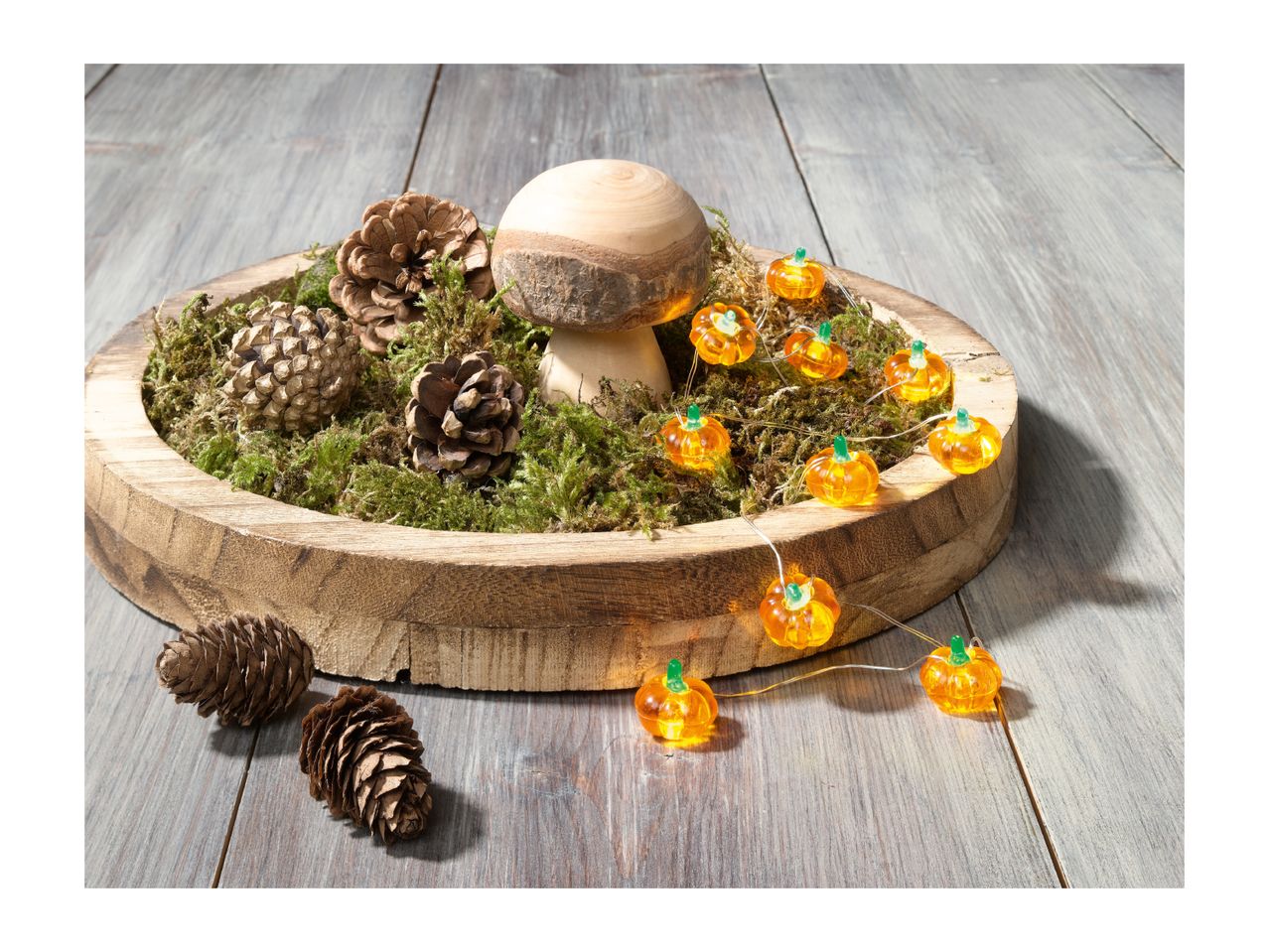 A wooden bowl with moss, pinecones, a wooden mushroom, and pumpkin string lights.