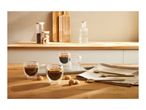 Espresso cups with coffee and cookies on a wooden counter, with kitchen items in the background.