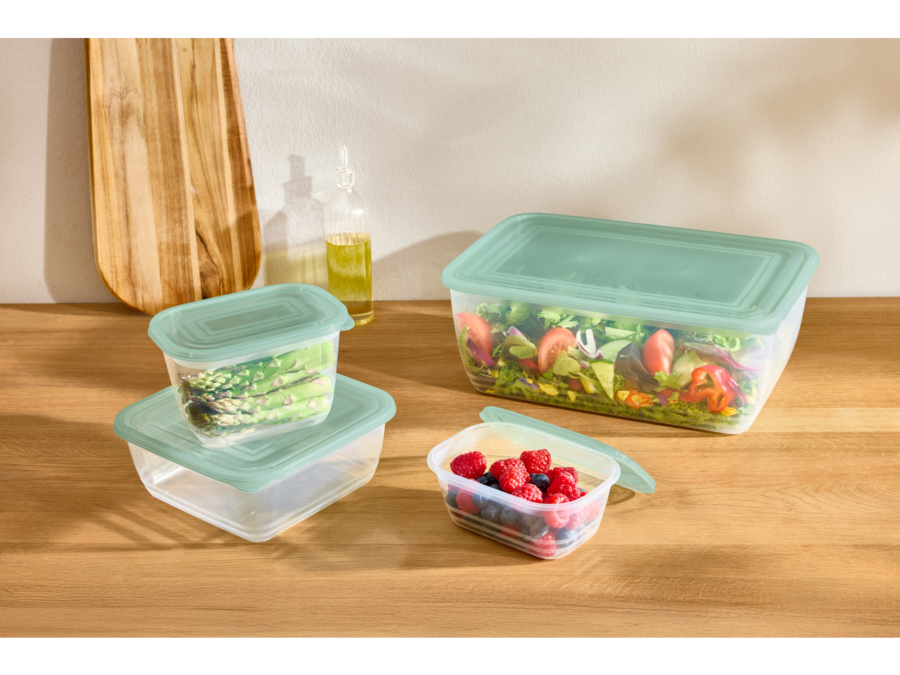 Kutije za čuvanje hrane sa svežom salatom, šparglama i bobičastim voćem na drvenom pultu.