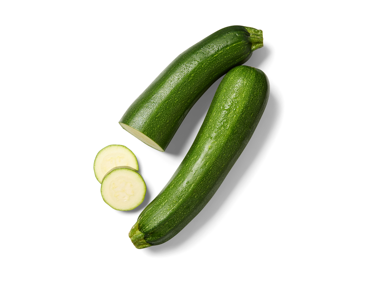 Twee verse groene courgettes, waarvan één gesneden in twee ronde plakjes, op een zwarte achtergrond.