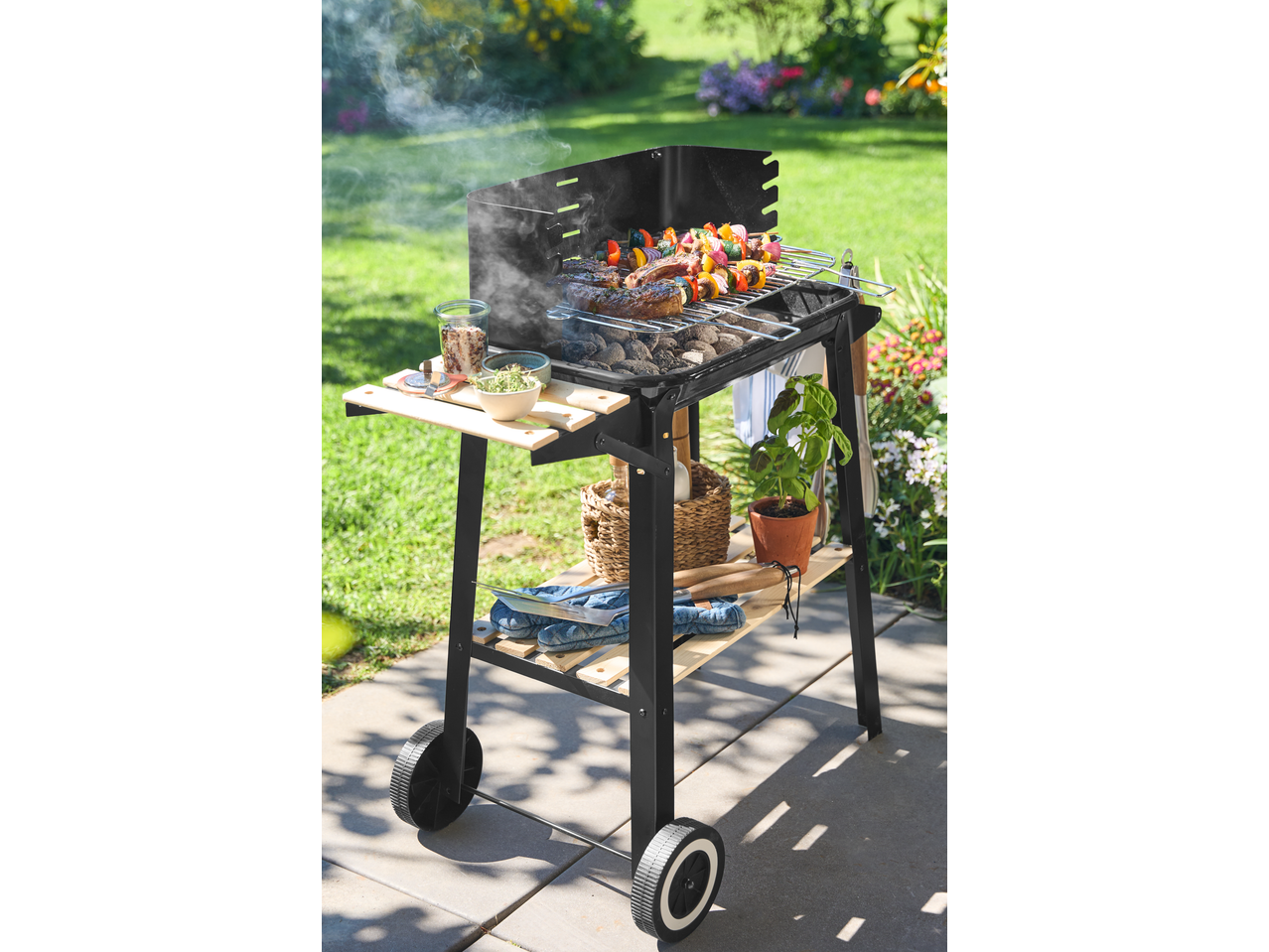 Barbecue grill with food cooking, side shelves, and storage, set in a garden.