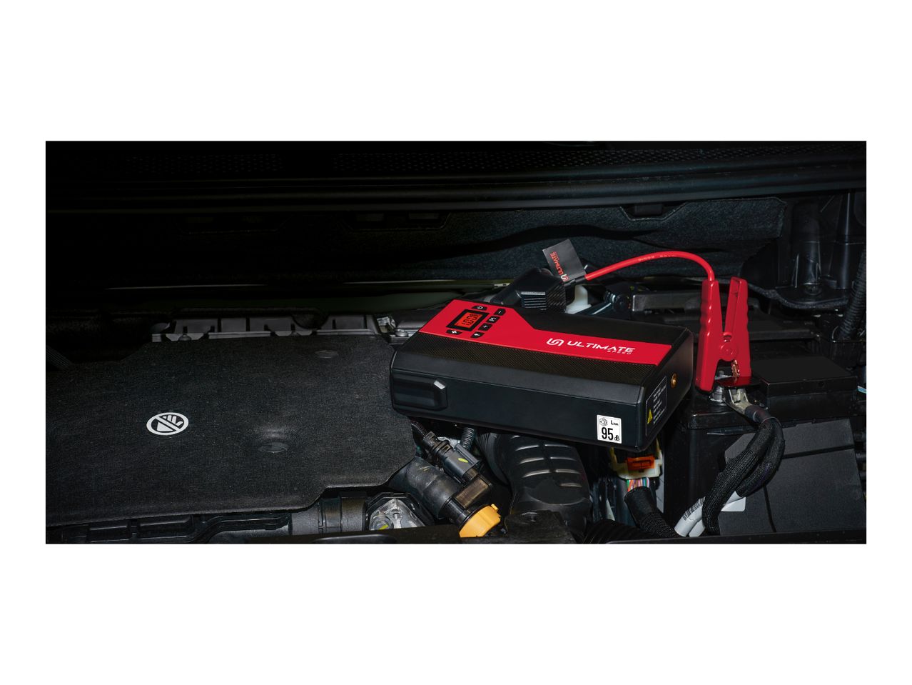 A red and black jump starter connected to a car battery under the hood.