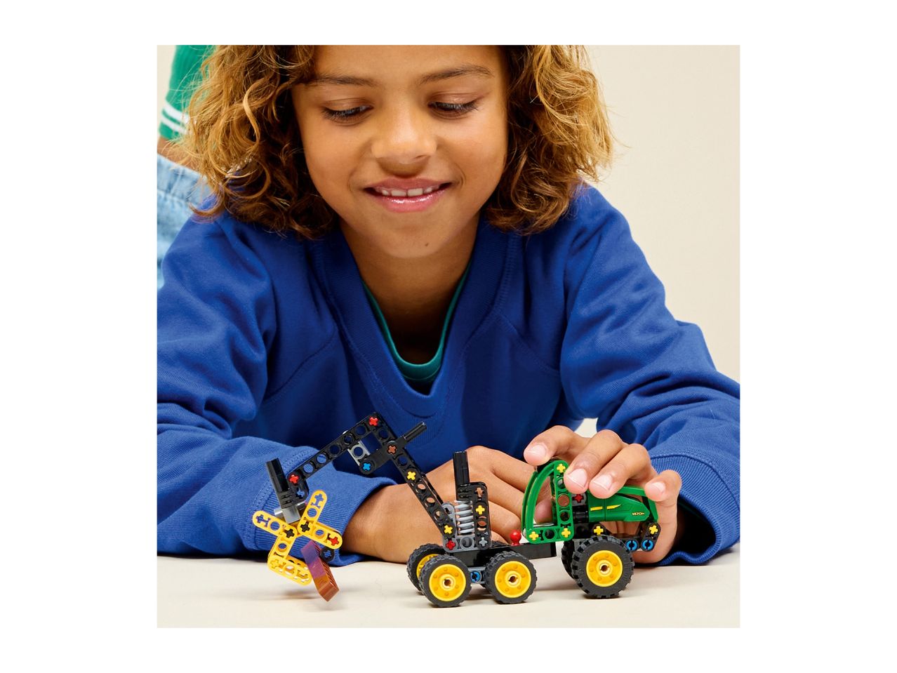 A child playing with a toy tractor and a toy crane made from building blocks.