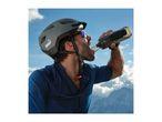 Cyclist in helmet and sunglasses drinking from a water bottle with mountains in background.