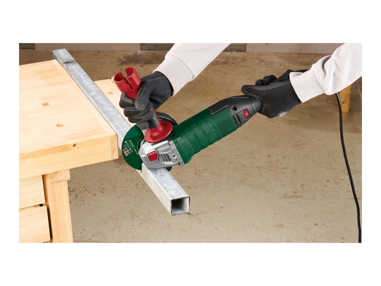 Person cutting a metal square tube with an angle grinder on a wooden workbench.