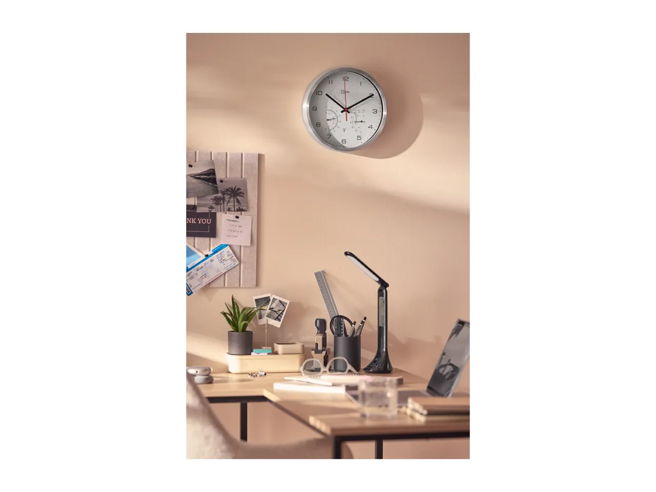 A modern wall clock hanging above a stylishly arranged desk with office accessories.