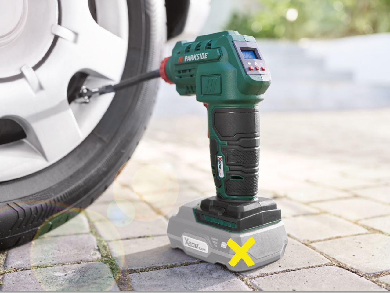 Roheline Parkside'i akukompressor pumpab auto rehvi sillutiskividel.