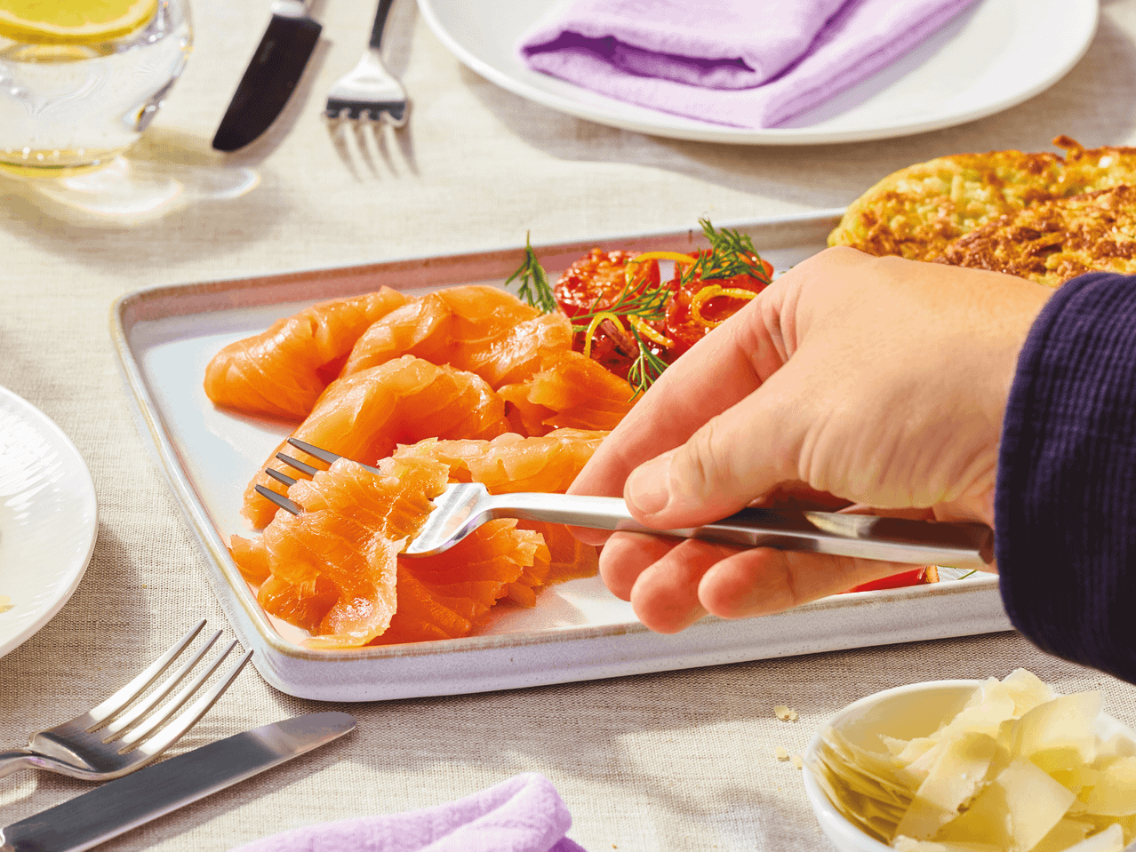Geräucherter Lachs auf einem Teller, mit einer Gabel aufgenommen, dazu Tomaten und Käse.