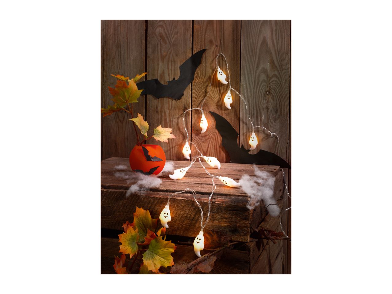 Halloween decorations with ghost lights, bats, and autumn leaves on a wooden background.