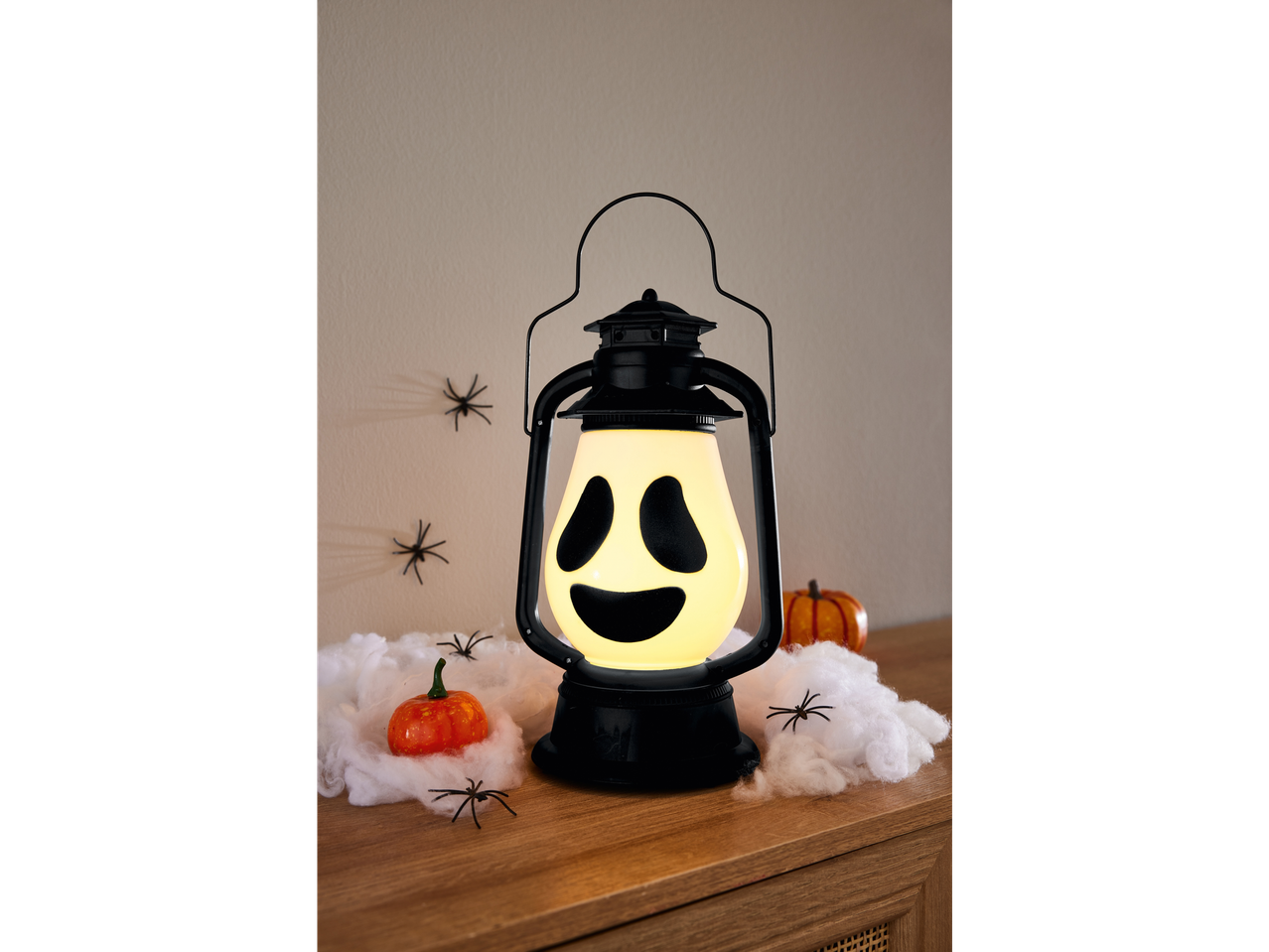 A Halloween lantern with a ghost face, surrounded by pumpkins and spiders.
