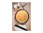 A freshly made crepe on a crepe maker, with flour, milk, and eggs nearby.