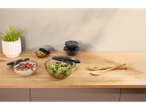 Tigelas de vidro com tampas, cheias de salada, frutas vermelhas e azeitonas, sobre uma bancada de madeira.