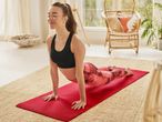 Woman in a black sports bra and red patterned leggings doing yoga on a red mat.