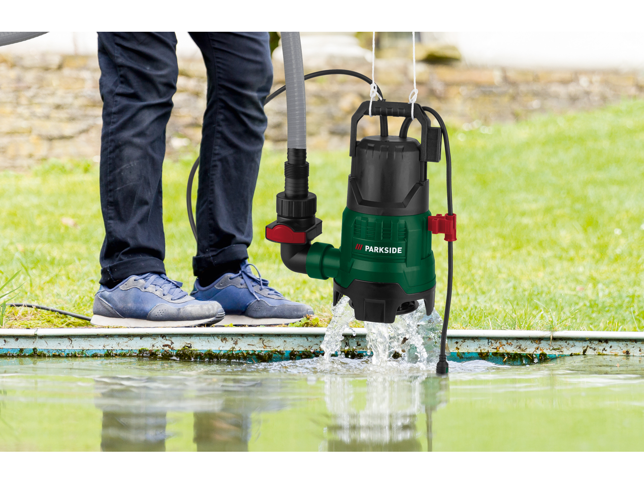 A person using a submersible pump to drain water from a pond in a garden.