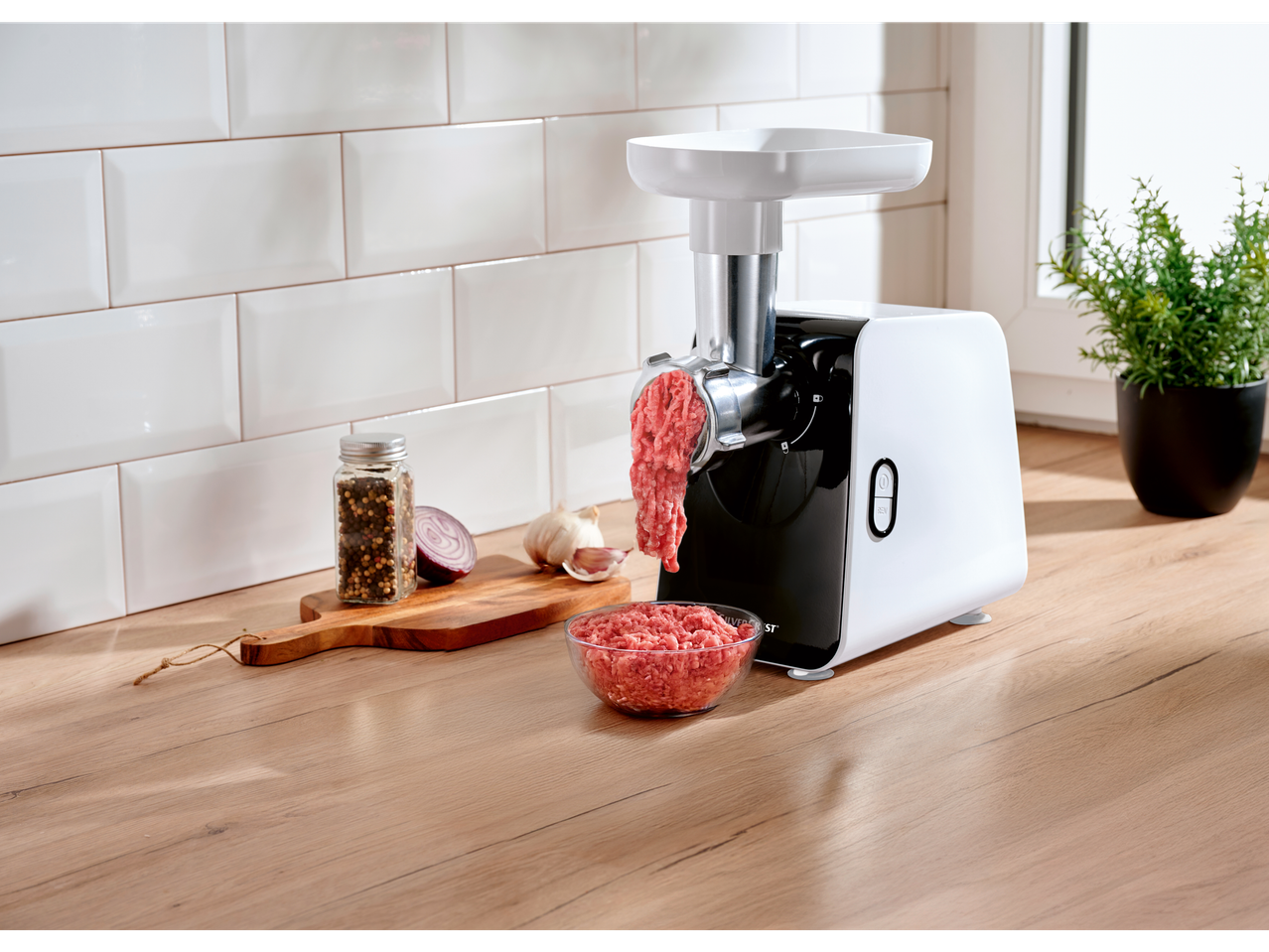Silvercrest® elektromos húsdaráló darál húst, fűszerekkel és hagymával egy vágódeszkán.