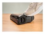 A foot pressing a release lever on a vacuum cleaner brush head.