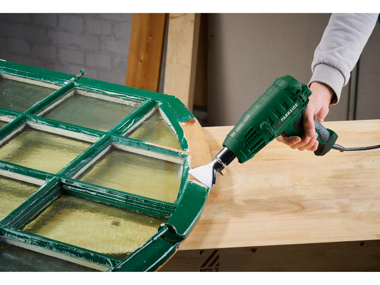 Egy személy Parkside forrólevegős pisztollyal javít egy régi ablakot.