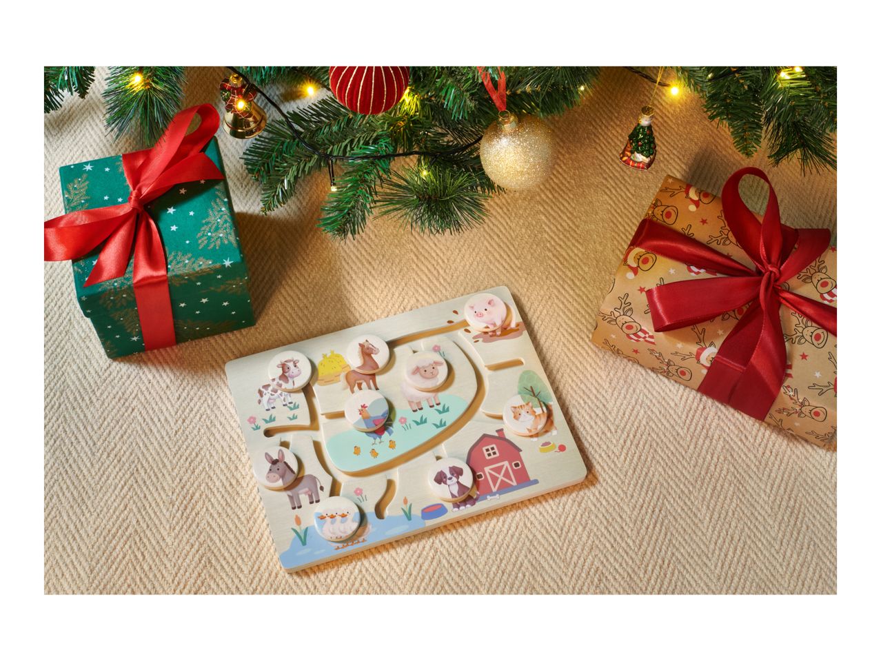 Christmas gifts and a farm animal puzzle on a beige blanket under a Christmas tree.