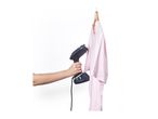 Handheld garment steamer being used on a pink t-shirt hanging on a wooden hanger.