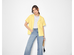 Mulher com blusa de musselina amarela ESMARA e jeans segurando uma clutch de palha.