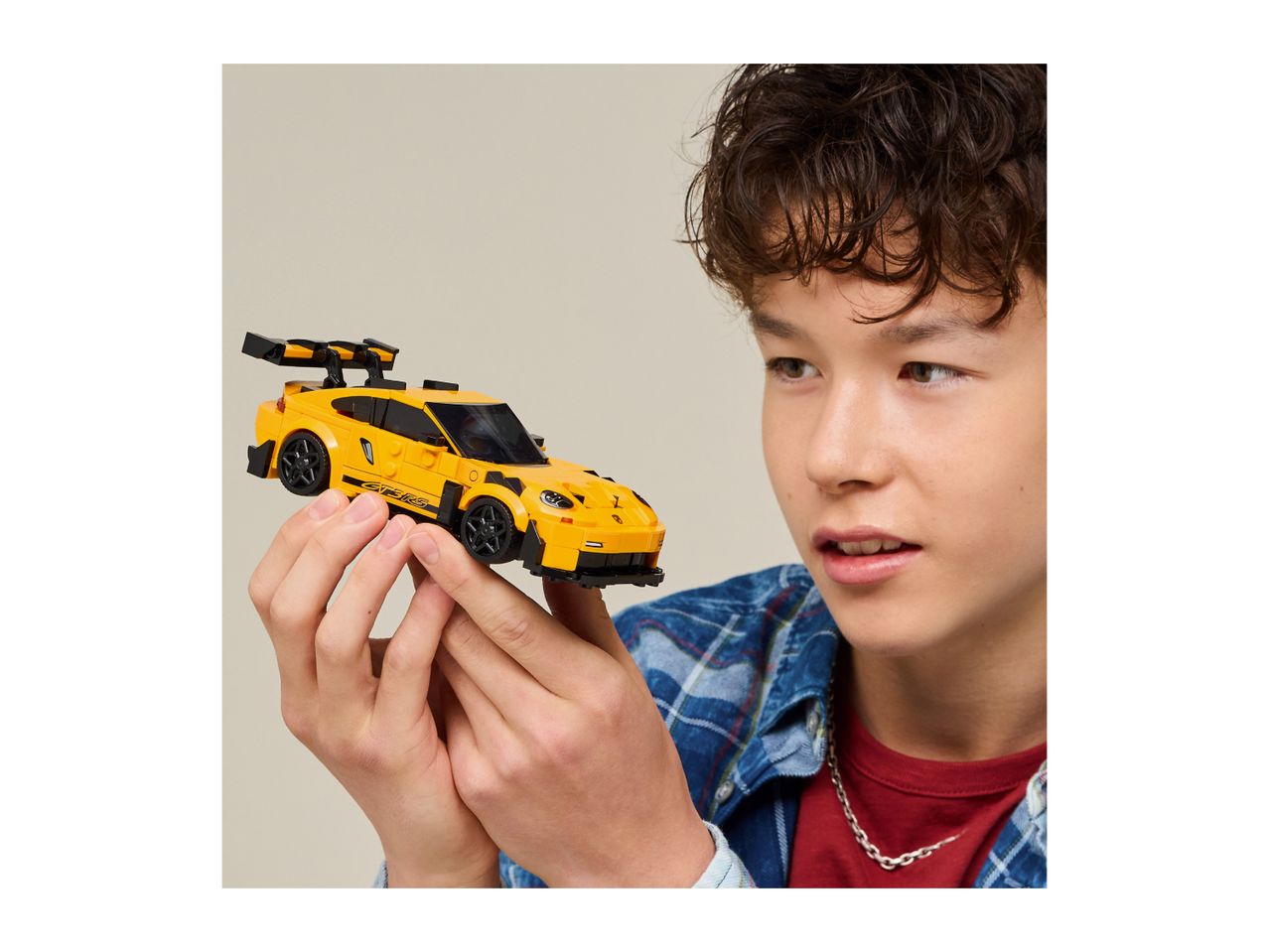 Boy holding a yellow toy sports car with a large rear spoiler.