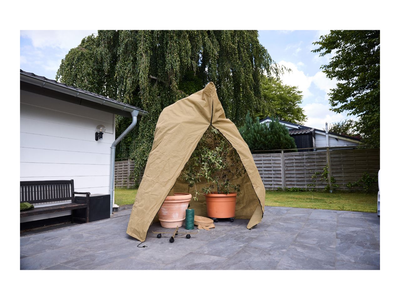 A protective plant cover tent sheltering potted plants on a patio.