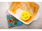 A smiley yellow sponge next to a dirty baking dish.