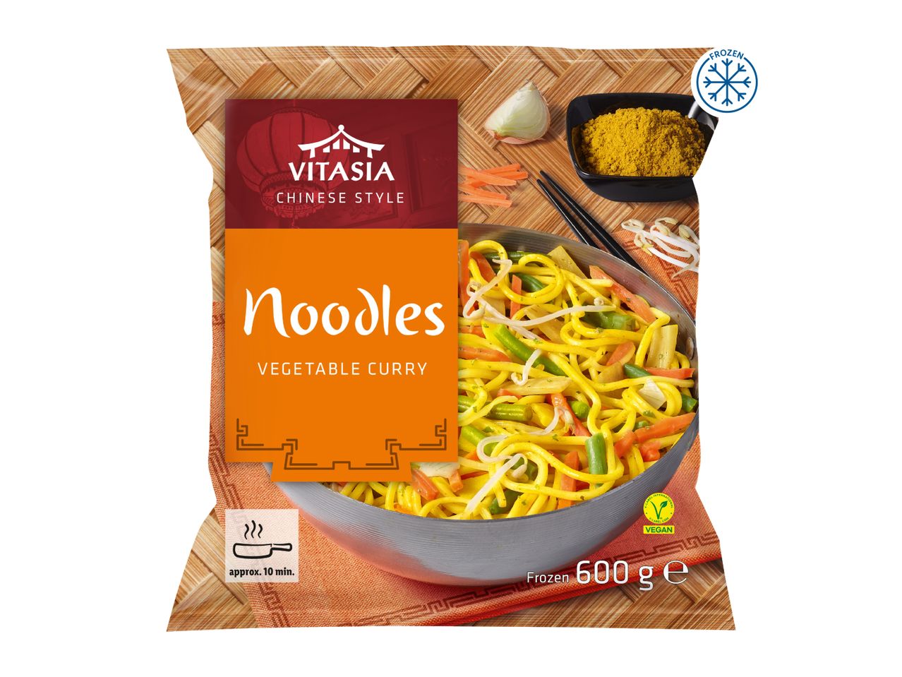 Frozen vegetable curry noodles in a bag, with a wok of noodles and ingredients on a bamboo mat.