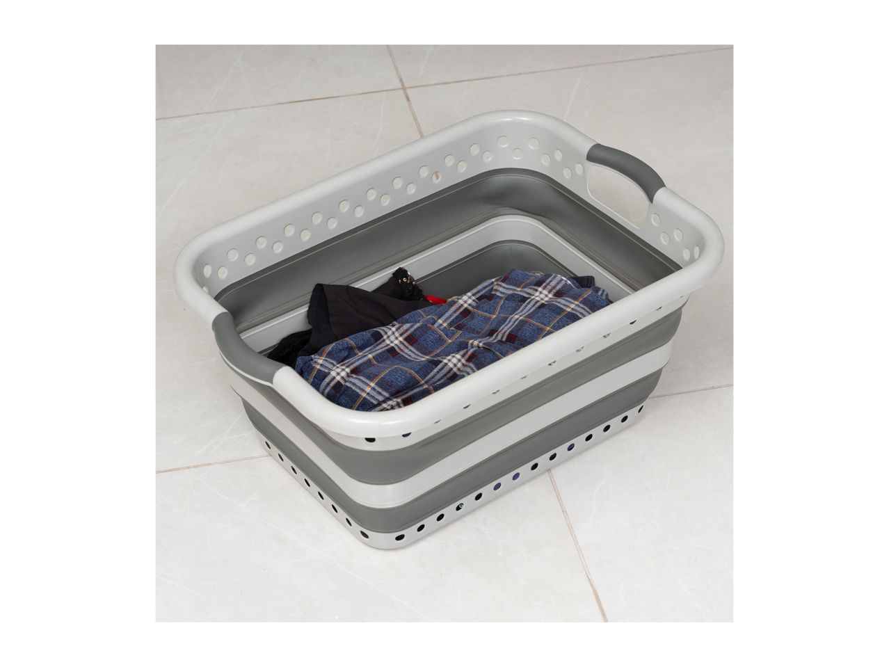 A gray and white collapsible laundry basket sits on a tiled floor, containing folded clothes.