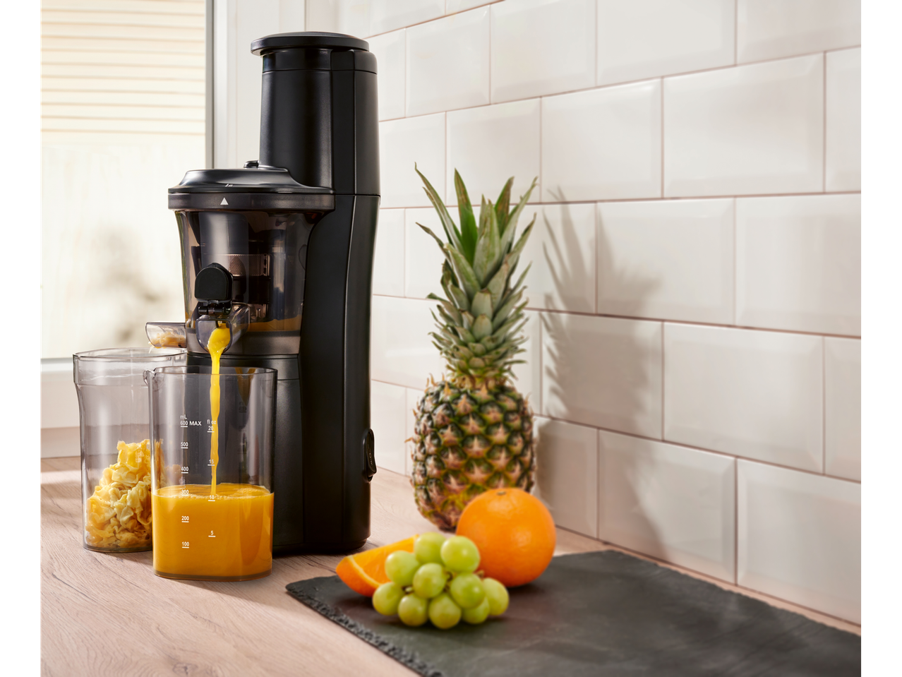 Silvercrest® slow juicer pouring juice into a glass, with pineapple and fruit.