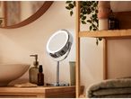 A chrome LED Make-Up Mirror on a wooden counter next to bathroom essentials.