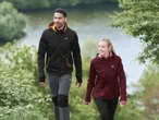 Zwei Personen in Outdoor-Jacken und -Hosen gehen einen Weg entlang.