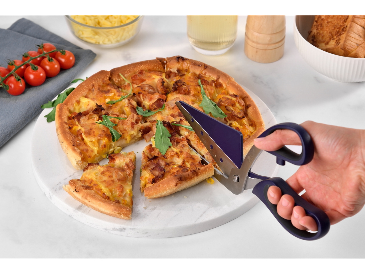 Pizza mit Käse und Speck wird mit einer Pizzatrennschere geschnitten.