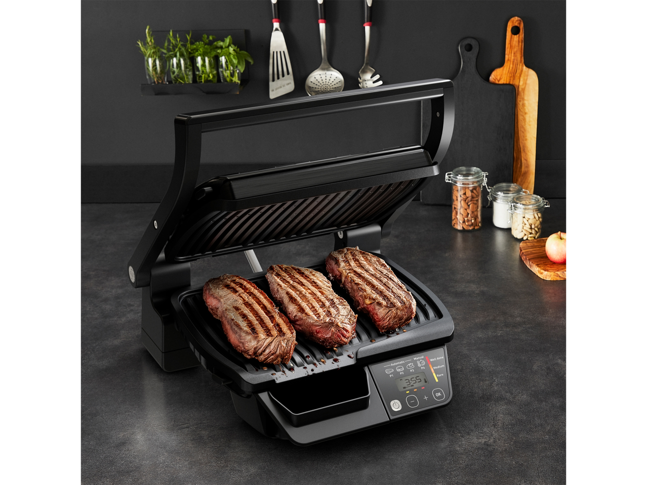 Grill Tefal cu trei fripturi la grătar și afișaj digital într-o bucătărie întunecată.