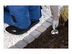 Person kneeling on a garden kneeler, planting next to a stone border with a trowel.