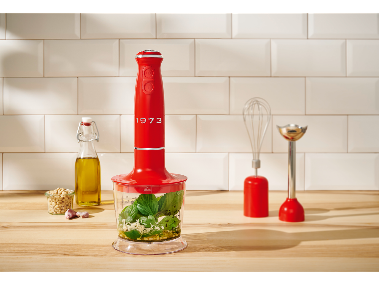Blender de mână roșu Silvercrest® 3 în 1 cu accesorii, pregătind pesto pe un blat de lemn.