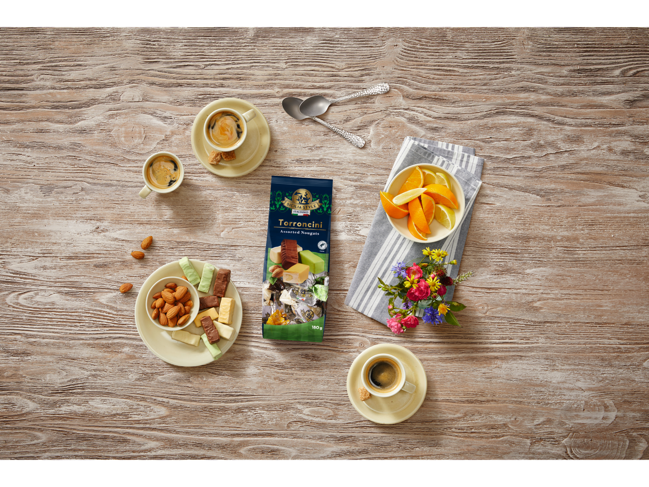 Een zak Sicilia Style Torroncini noga, koffie, amandelen, fruit en bloemen op een houten tafel.