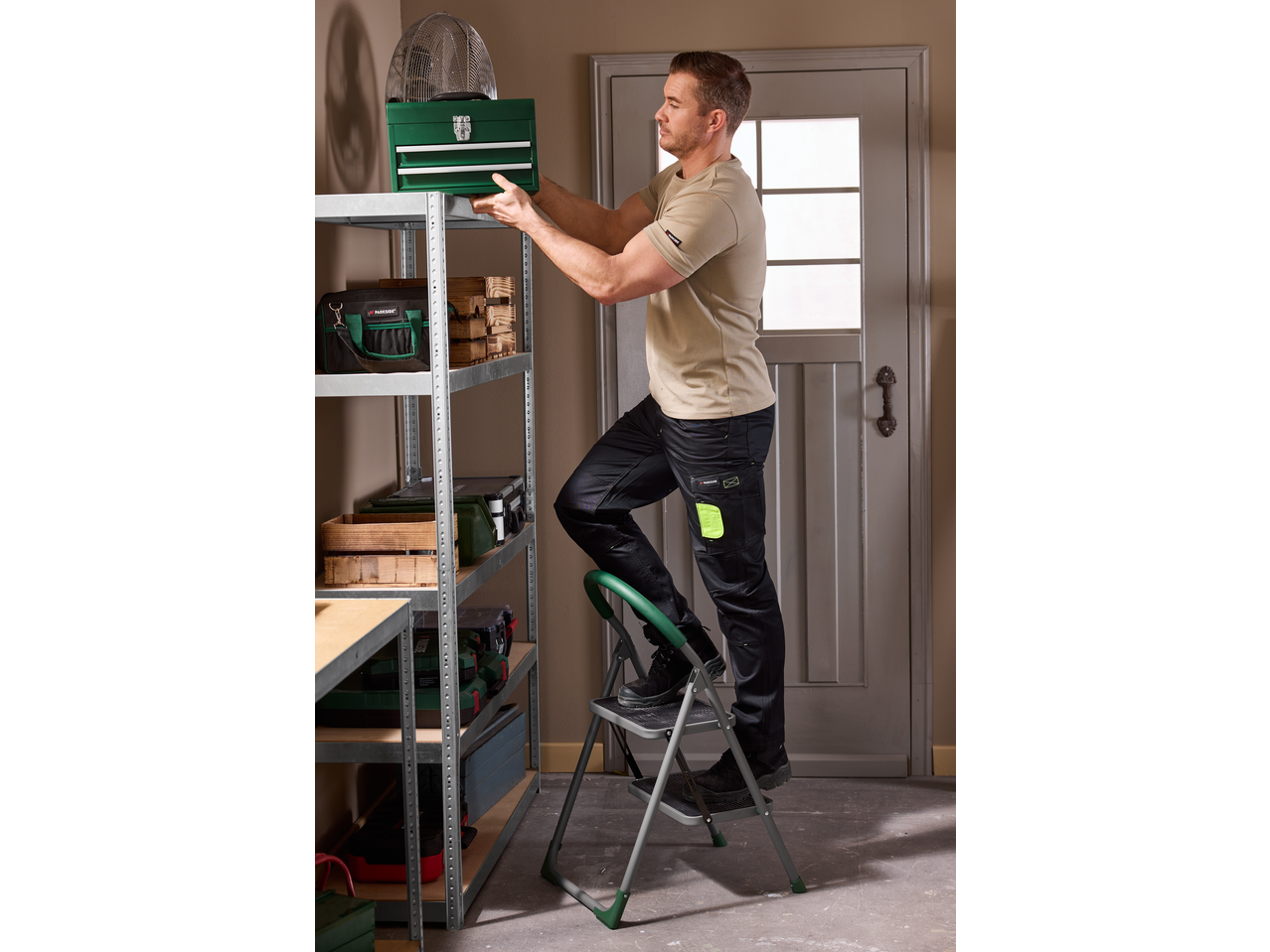 Muškarac na PARKSIDE ljestvama postavlja kutiju s alatom na policu.