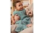 Baby in teal sleep sack with wooden rattle.