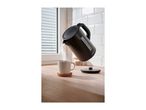 Black kettle pouring hot water into a white mug on a wooden countertop.