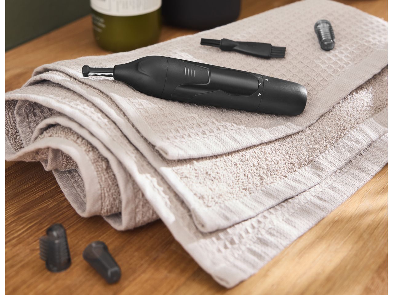 Black electric trimmer with accessories on a folded beige towel on a wooden surface.
