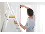 Man on ladder using a PARKSIDE® Laser Distance Measurer to measure a window frame.