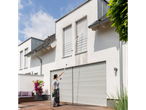 Woman cleaning house facade and roller shutters with a pressure washer and telescopic lance.