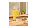 Yellow travel mug with a straw and handle on a wooden counter next to cookies.