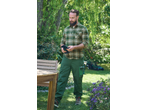 Man in green plaid shirt and work trousers holding gardening gloves in a garden.