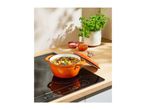 An orange cast iron pot filled with stew on a black induction cooktop.