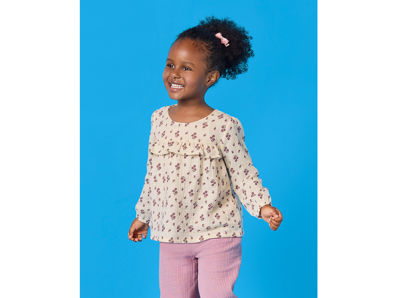 Fetiță în bluză de muselină LUPILU și pantaloni roz, zâmbind.