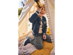 A boy plays with a telescope inside a teepee wearing a navy blue bomber jacket and grey jeans.