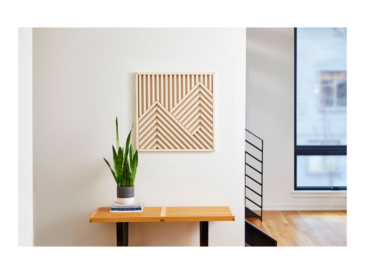 A modern wooden slatted bench with a potted snake plant and geometric wall art.