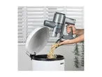A person empties a handheld vacuum cleaner into a white bin, with white blinds in the background.